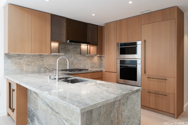 kitchen featuring decorative backsplash, light hardwood / wood-style floors, light stone counters, and double oven