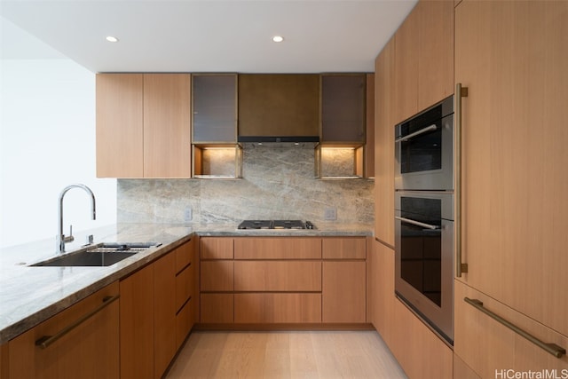 kitchen with light stone countertops, sink, light hardwood / wood-style flooring, backsplash, and appliances with stainless steel finishes