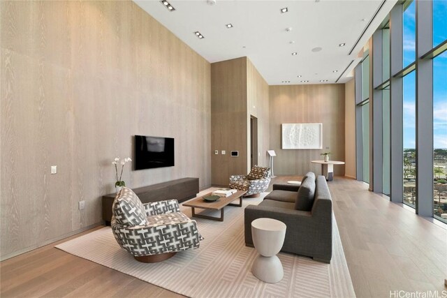 living room featuring a towering ceiling, light hardwood / wood-style floors, and a wall of windows