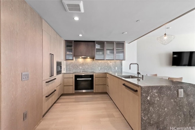 kitchen featuring light brown cabinets, black appliances, sink, wall chimney exhaust hood, and light hardwood / wood-style floors