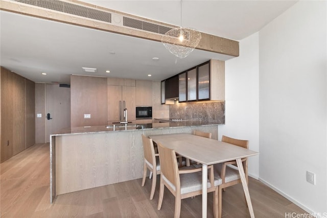 kitchen with light hardwood / wood-style flooring, decorative backsplash, light stone countertops, decorative light fixtures, and kitchen peninsula