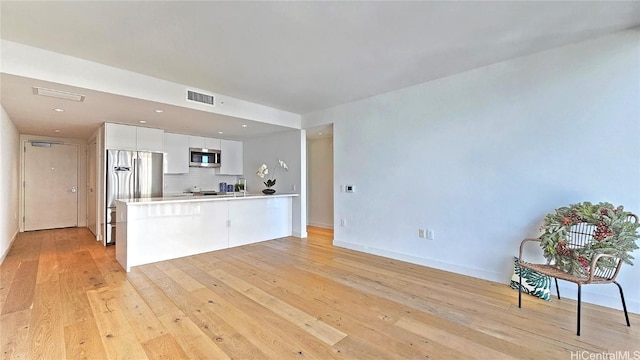 kitchen with light hardwood / wood-style flooring, backsplash, kitchen peninsula, white cabinets, and appliances with stainless steel finishes