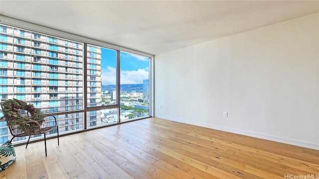 empty room with a city view, a wall of windows, light wood-style flooring, and baseboards