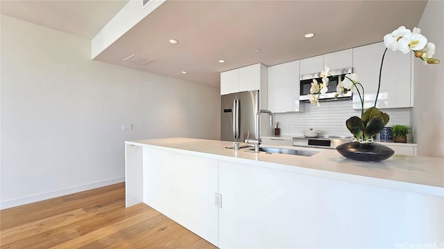 kitchen with tasteful backsplash, light wood-type flooring, appliances with stainless steel finishes, white cabinetry, and a sink