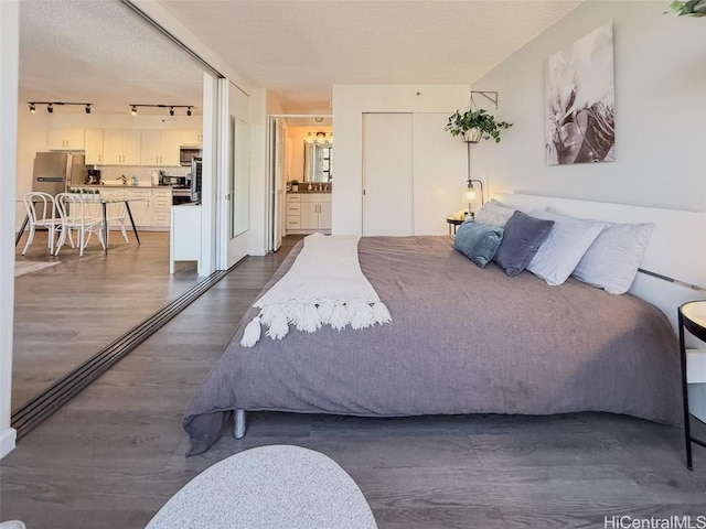 bedroom featuring dark wood-type flooring, track lighting, stainless steel fridge, connected bathroom, and a closet