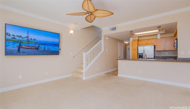 unfurnished living room featuring light colored carpet, a ceiling fan, baseboards, stairs, and crown molding