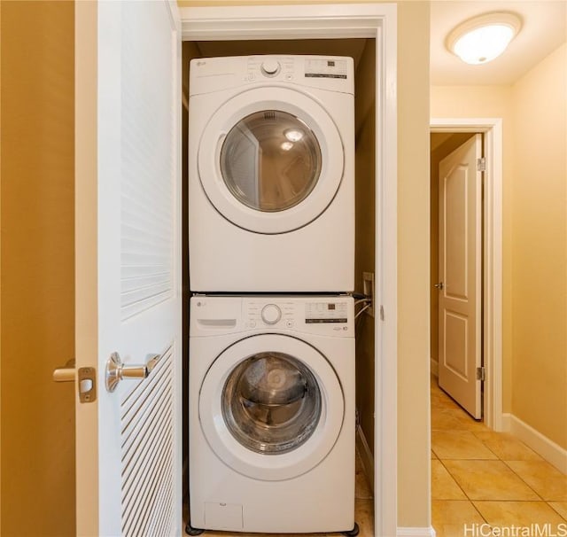 laundry area with laundry area, baseboards, light tile patterned flooring, and stacked washer and clothes dryer