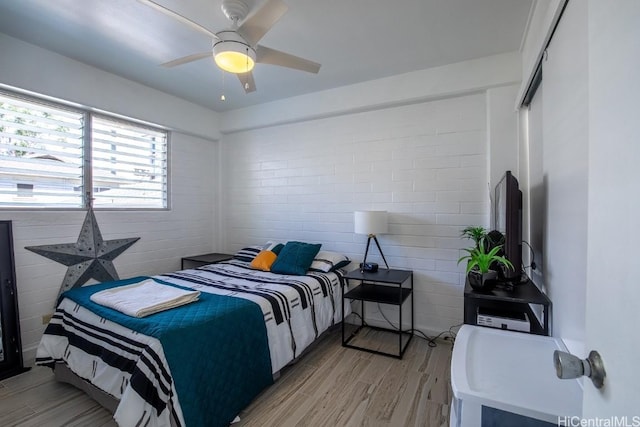 bedroom featuring ceiling fan, light hardwood / wood-style floors, and brick wall