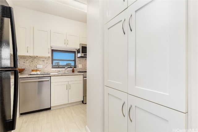 kitchen featuring light stone countertops, appliances with stainless steel finishes, tasteful backsplash, sink, and white cabinetry