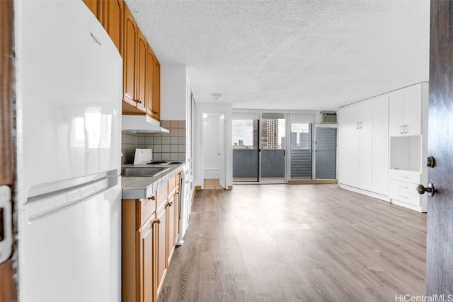 kitchen featuring tile countertops, decorative backsplash, light wood-type flooring, a textured ceiling, and white fridge