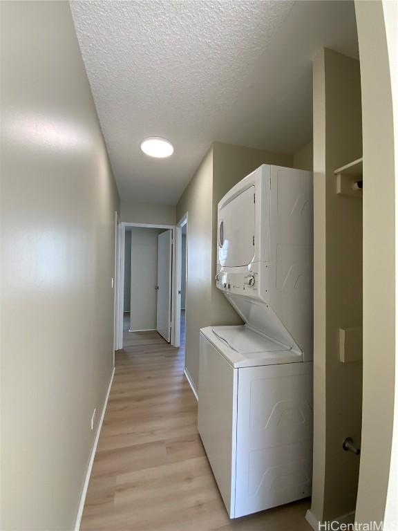 laundry area with a textured ceiling, light hardwood / wood-style floors, and stacked washer / dryer