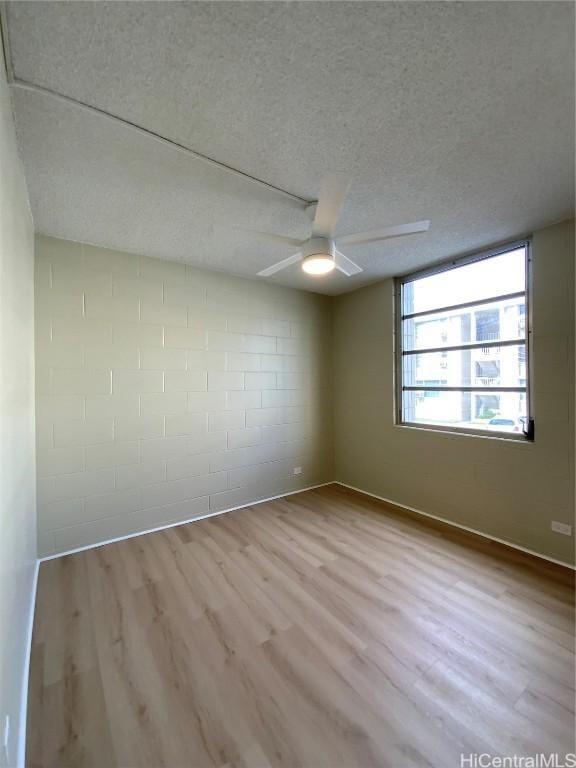 empty room with a textured ceiling, light wood-type flooring, and ceiling fan