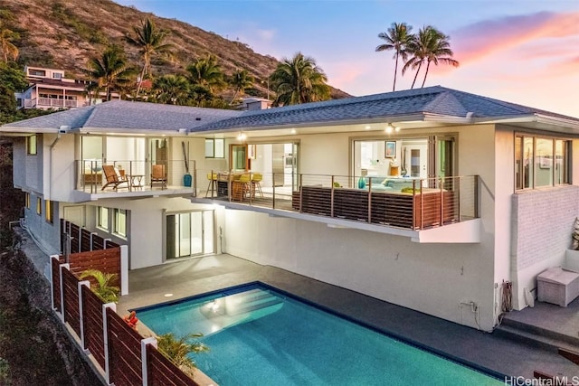 back house at dusk featuring a mountain view, a patio, a balcony, and a fenced in pool