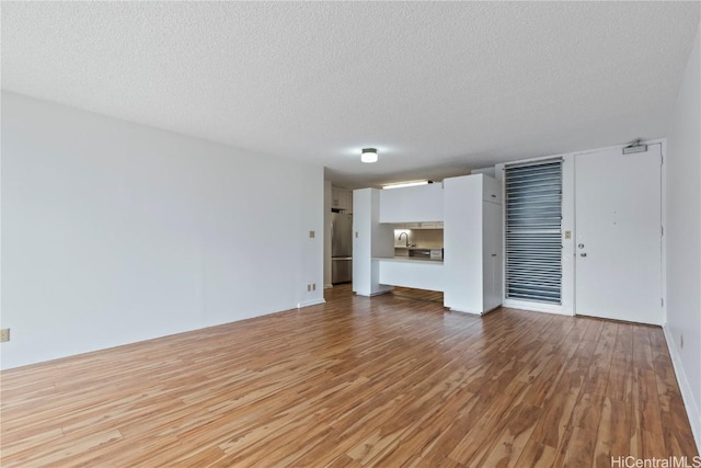 unfurnished living room with light hardwood / wood-style flooring and a textured ceiling