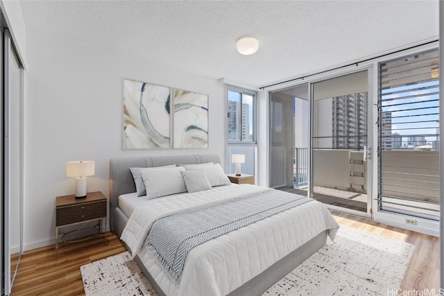 bedroom with hardwood / wood-style flooring, a wall of windows, a textured ceiling, and a closet