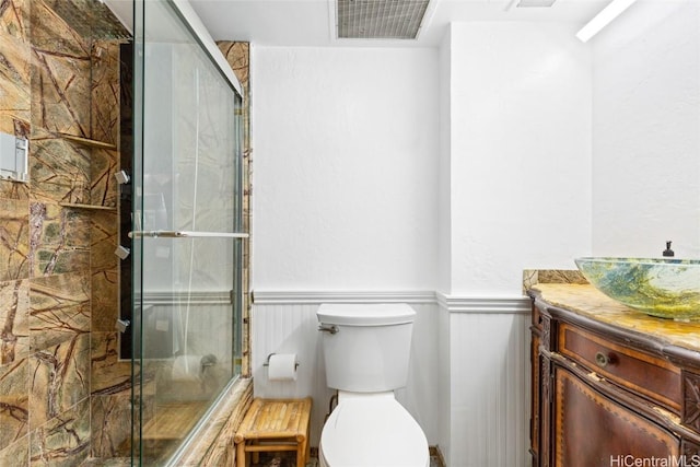 bathroom featuring a shower with shower door, visible vents, vanity, and wainscoting