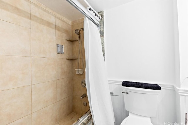 bathroom featuring a decorative wall, toilet, a tile shower, and wainscoting