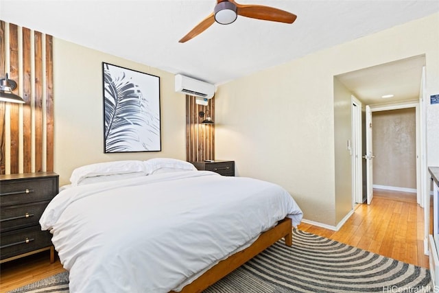 bedroom featuring light wood-type flooring, baseboards, a ceiling fan, and a wall unit AC