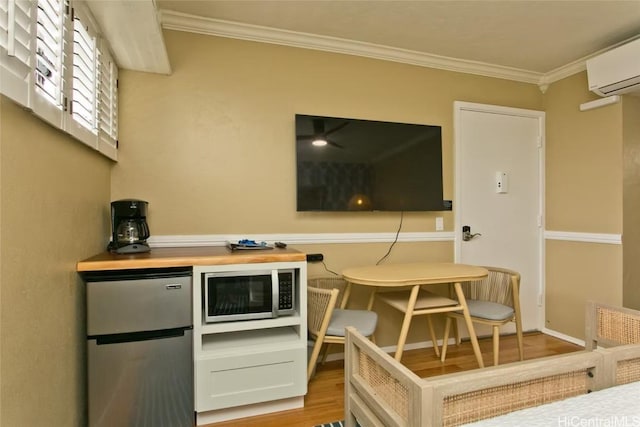 interior space with butcher block countertops, light wood-style flooring, a wall mounted AC, stainless steel appliances, and crown molding