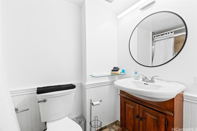 bathroom featuring a wainscoted wall, toilet, and vanity