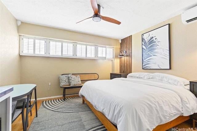 bedroom featuring ceiling fan, wood finished floors, baseboards, and a wall mounted AC