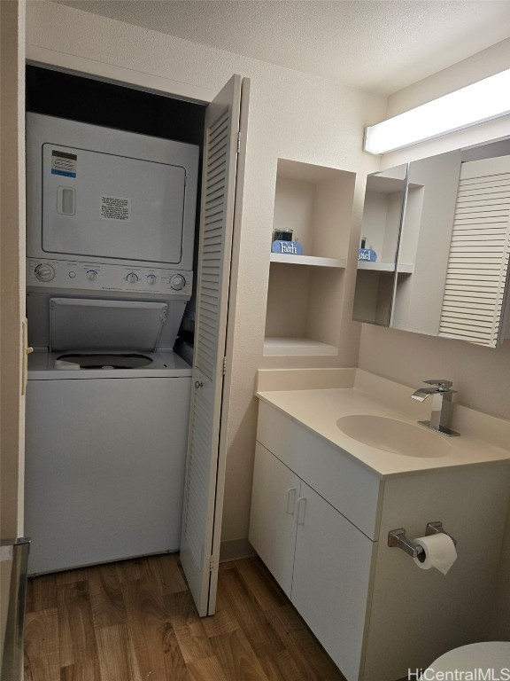 laundry room with sink, stacked washer and clothes dryer, dark wood-type flooring, and a textured ceiling