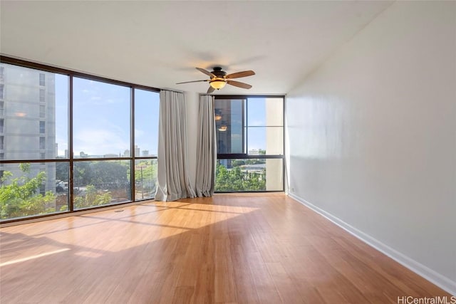 unfurnished room featuring expansive windows, light hardwood / wood-style floors, plenty of natural light, and ceiling fan