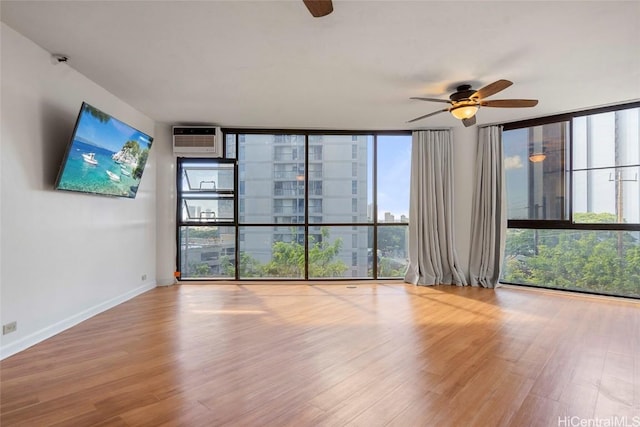 unfurnished room featuring a wall unit AC, ceiling fan, light hardwood / wood-style flooring, and a wall of windows