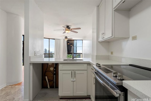 kitchen with stainless steel electric stove, white cabinetry, sink, and ceiling fan