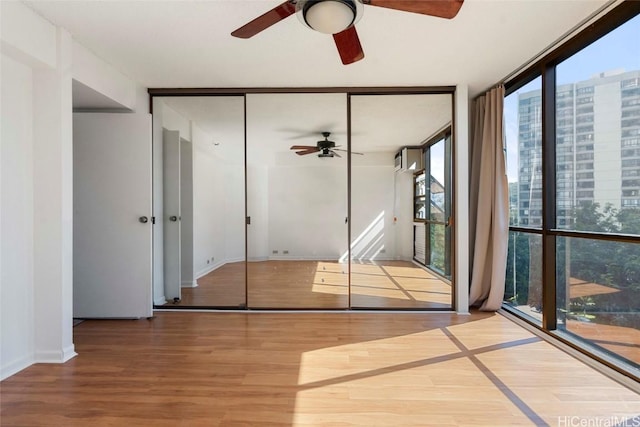 unfurnished bedroom featuring ceiling fan, a closet, wood-type flooring, and a wall of windows