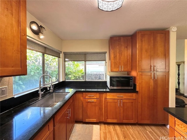 kitchen featuring a textured ceiling, light hardwood / wood-style floors, dark stone counters, and sink