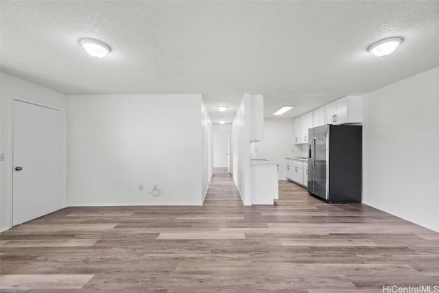 kitchen featuring stainless steel fridge, a textured ceiling, light hardwood / wood-style flooring, and white cabinetry