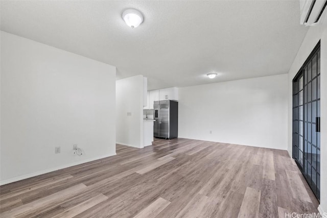 unfurnished living room featuring a wall mounted air conditioner, a textured ceiling, and light hardwood / wood-style floors