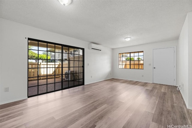 empty room featuring a wall mounted air conditioner, a baseboard radiator, light hardwood / wood-style floors, and a textured ceiling