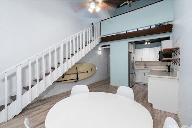 dining space with a high ceiling, light hardwood / wood-style floors, ceiling fan, and sink