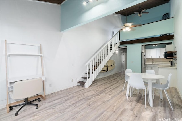 dining space featuring ceiling fan, sink, light hardwood / wood-style floors, and a high ceiling