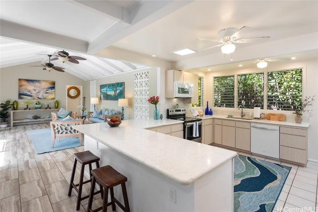 kitchen featuring sink, lofted ceiling with beams, kitchen peninsula, white appliances, and a kitchen bar