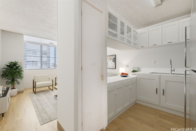 kitchen with light stone countertops, white cabinetry, sink, light hardwood / wood-style floors, and a textured ceiling