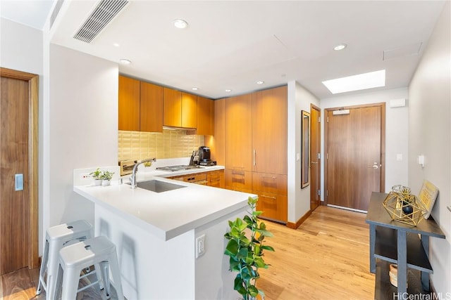 kitchen featuring kitchen peninsula, decorative backsplash, a breakfast bar, sink, and light hardwood / wood-style floors