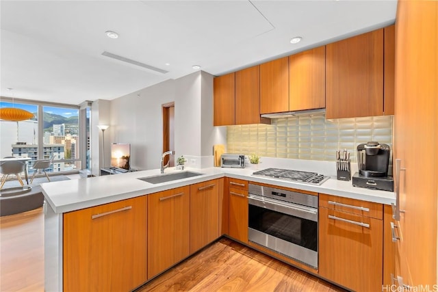 kitchen featuring sink, stainless steel appliances, tasteful backsplash, kitchen peninsula, and light wood-type flooring