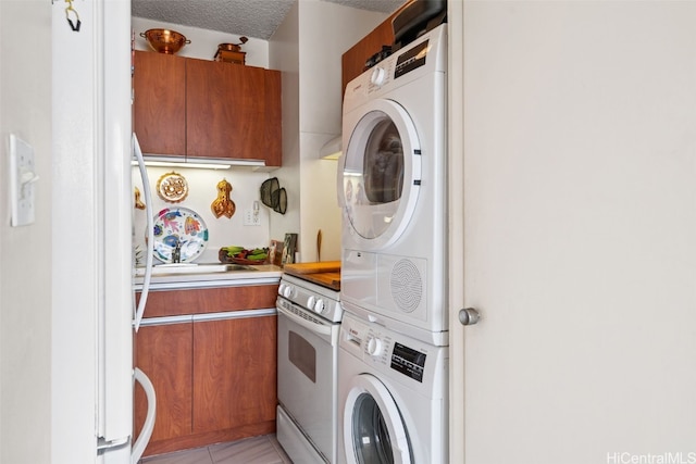 laundry room featuring sink, light tile patterned floors, stacked washing maching and dryer, and a textured ceiling