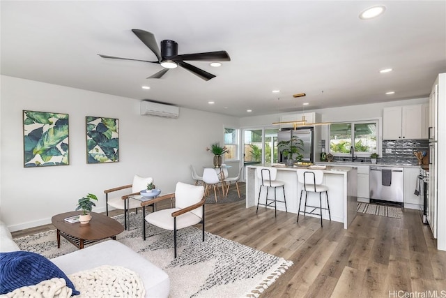 living room with ceiling fan, sink, light hardwood / wood-style floors, and a wall mounted air conditioner