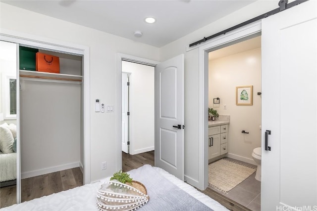 bedroom featuring a barn door, ensuite bathroom, a closet, and dark hardwood / wood-style floors