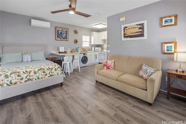 bedroom with a wall unit AC, ceiling fan, wood-type flooring, and washer / dryer