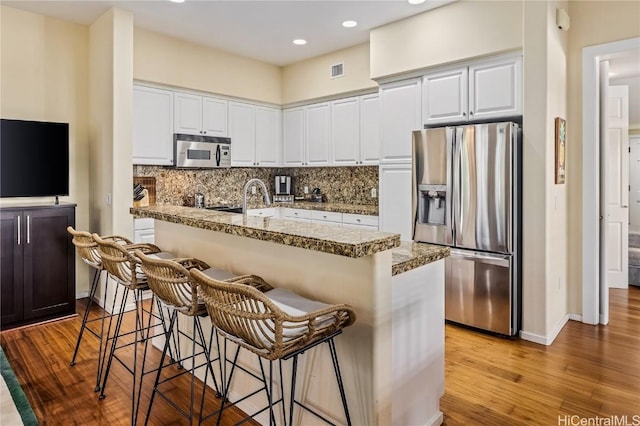 kitchen featuring a kitchen bar, appliances with stainless steel finishes, decorative backsplash, light hardwood / wood-style flooring, and white cabinetry