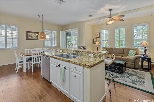 kitchen featuring white cabinetry, sink, a healthy amount of sunlight, stainless steel dishwasher, and decorative light fixtures