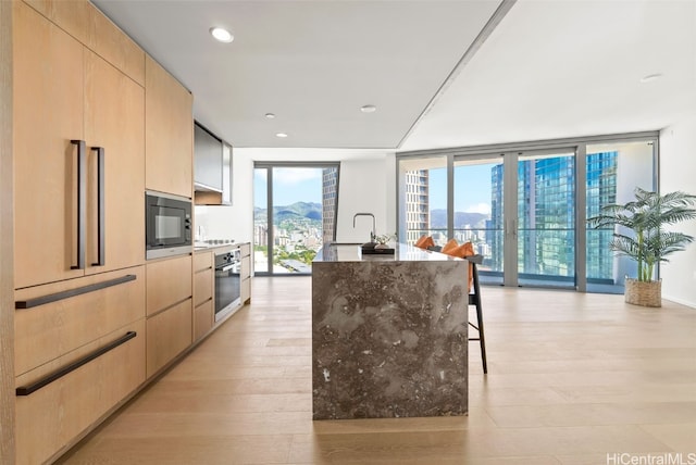 kitchen featuring built in microwave, light brown cabinetry, expansive windows, and stainless steel oven