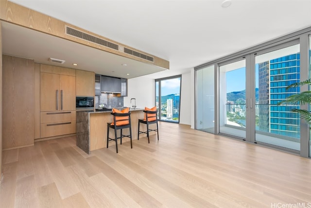 kitchen featuring decorative backsplash, light wood-type flooring, a breakfast bar, stainless steel microwave, and an island with sink