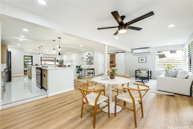 dining room with ceiling fan, a barn door, a wall mounted AC, and light hardwood / wood-style flooring