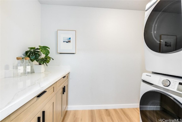 laundry room with cabinets, light hardwood / wood-style floors, and stacked washer and clothes dryer